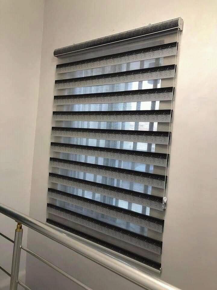 Grey day & night blind fitted on a stairwell landing, sheer and solid bands aligned